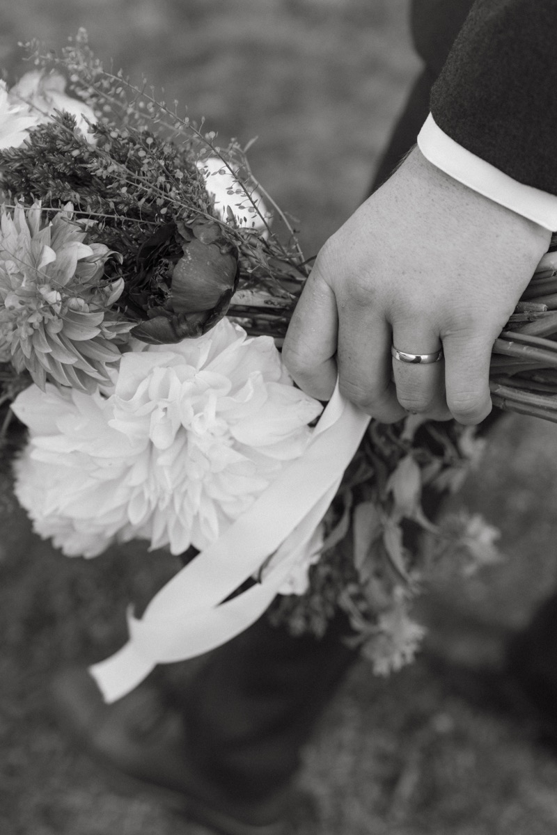 Groom’s hand with his ring on the bride’s bouquet in black and white