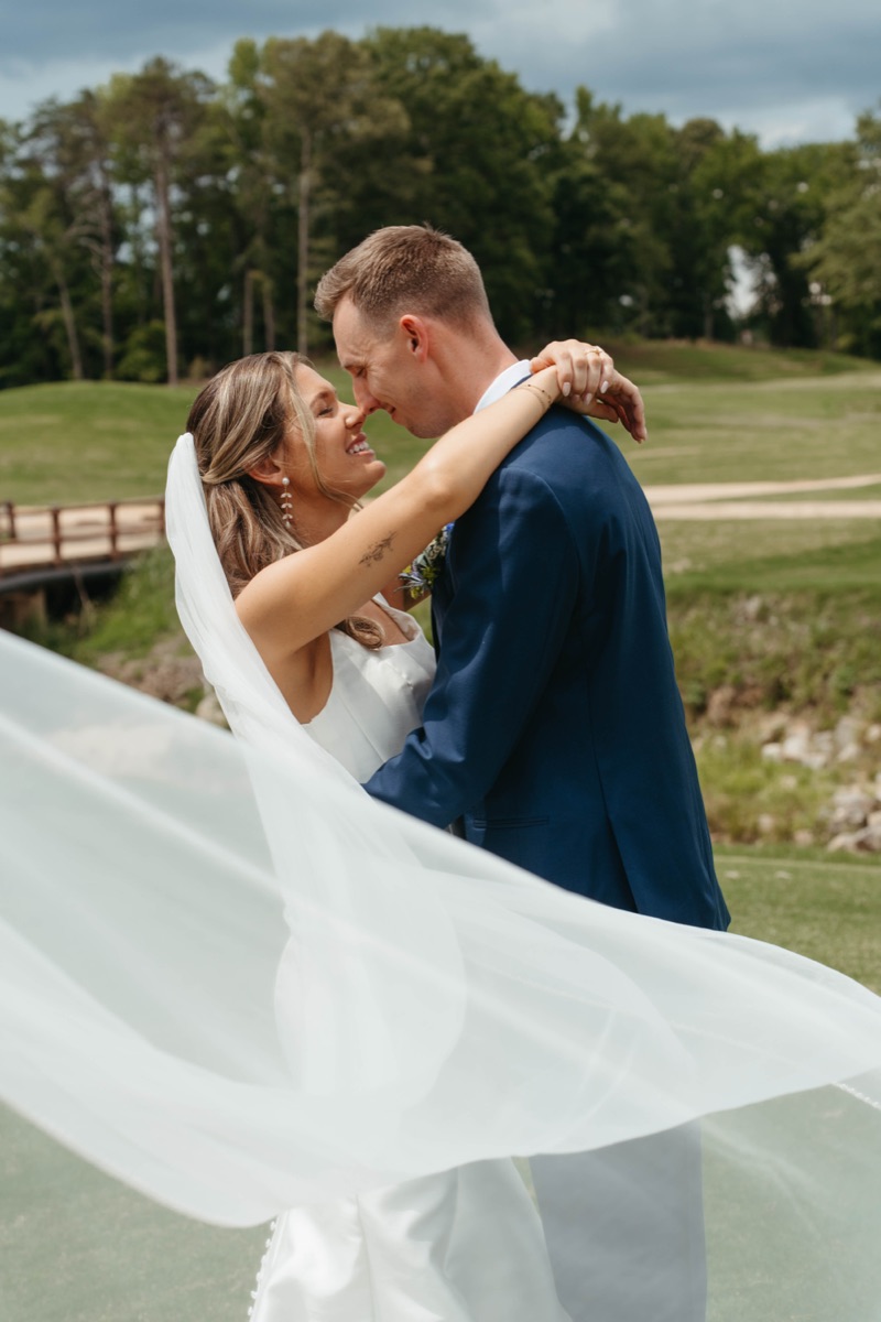 Bride and groom kissing as her veil catches the wind