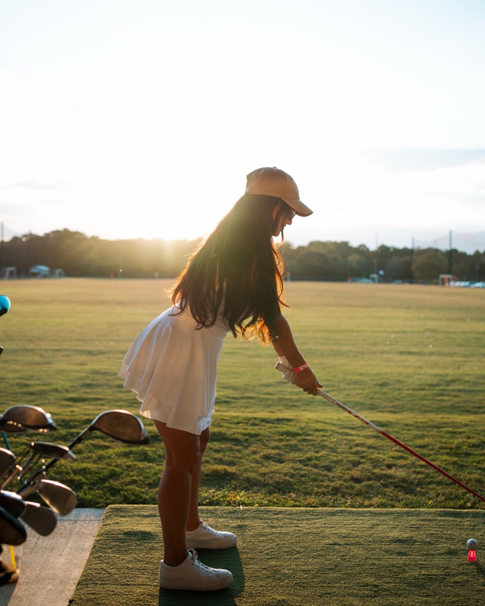 Woman lining up a golf shot at sunset